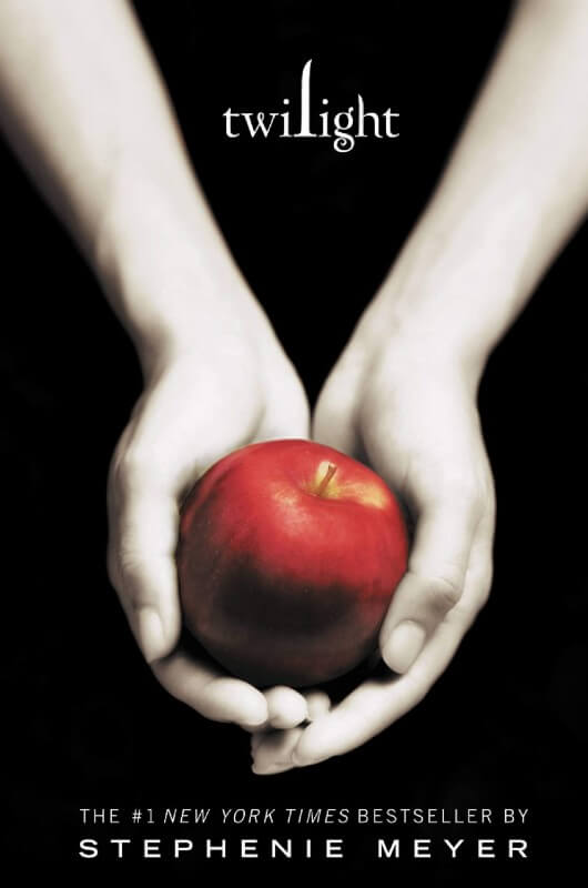 A black book cover that reads "Twilight: The #1 New York Times Bestseller by Stephanie Meyer". A pair of pale hands profer a whole red apple